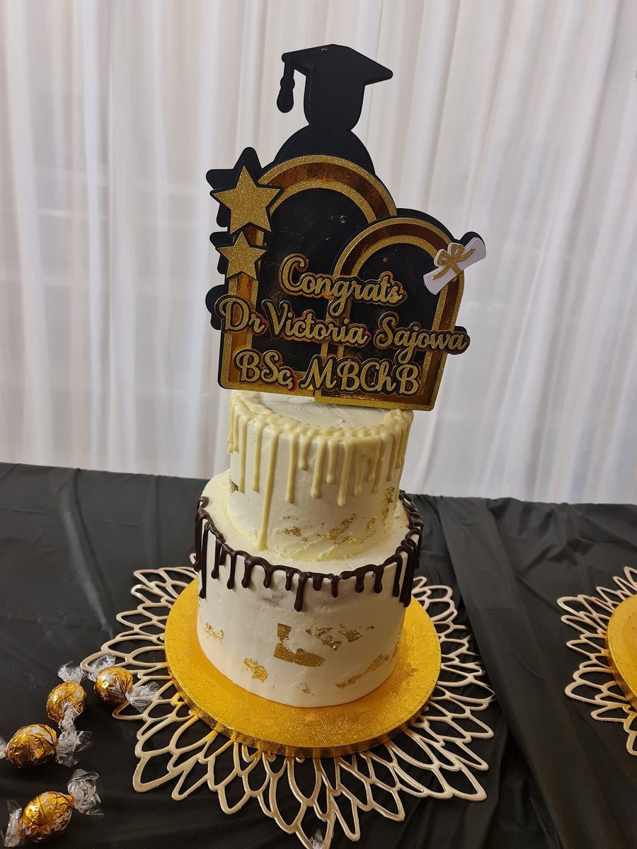 Two-tier white and gold graduation drip cake with a Congrats Dr topper, by Kakes by Grace in Plaistow