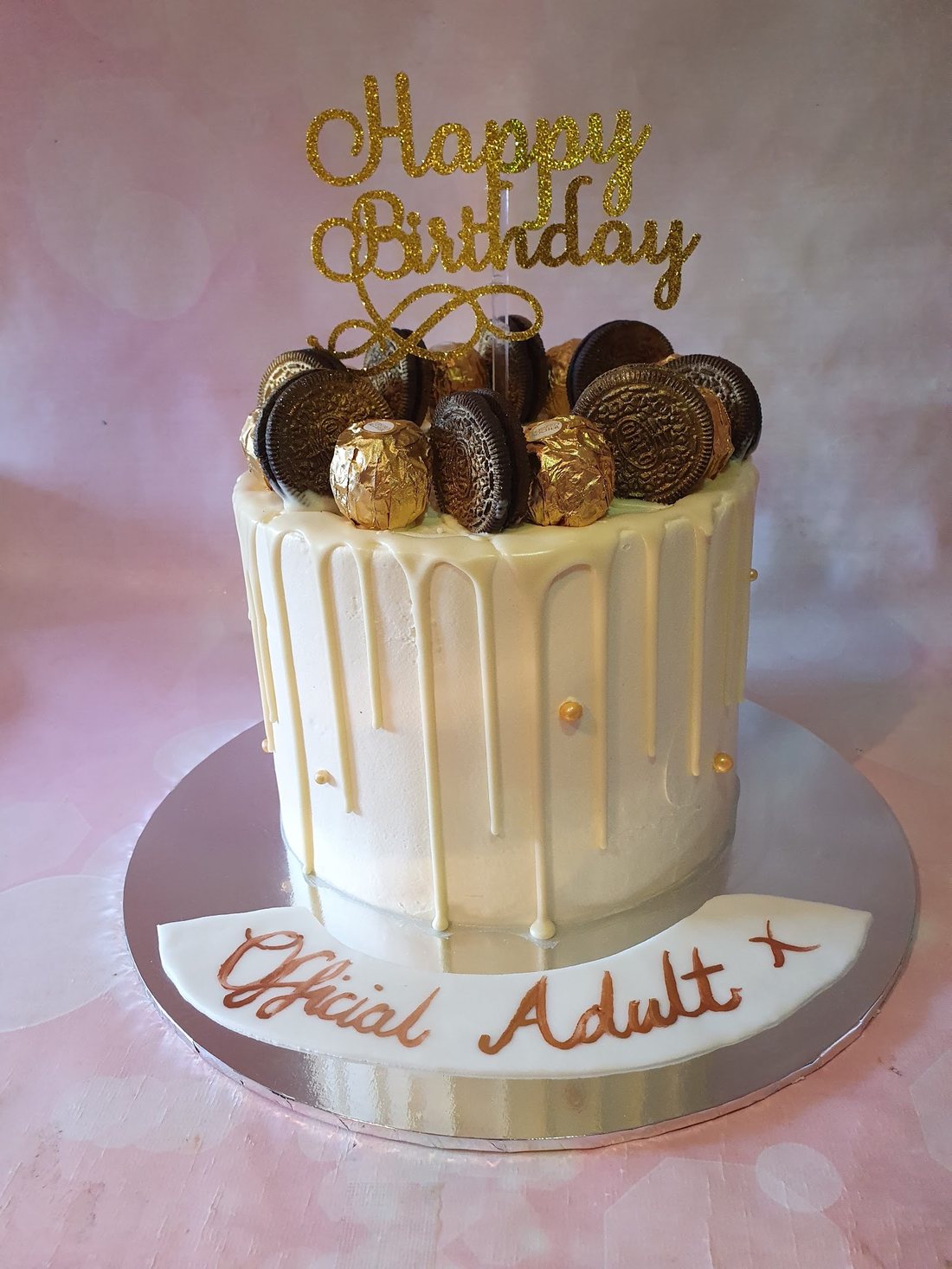A white chocolate drip celebration cake topped with Oreos and gold-wrapped chocolates, made by Kakes by Grace